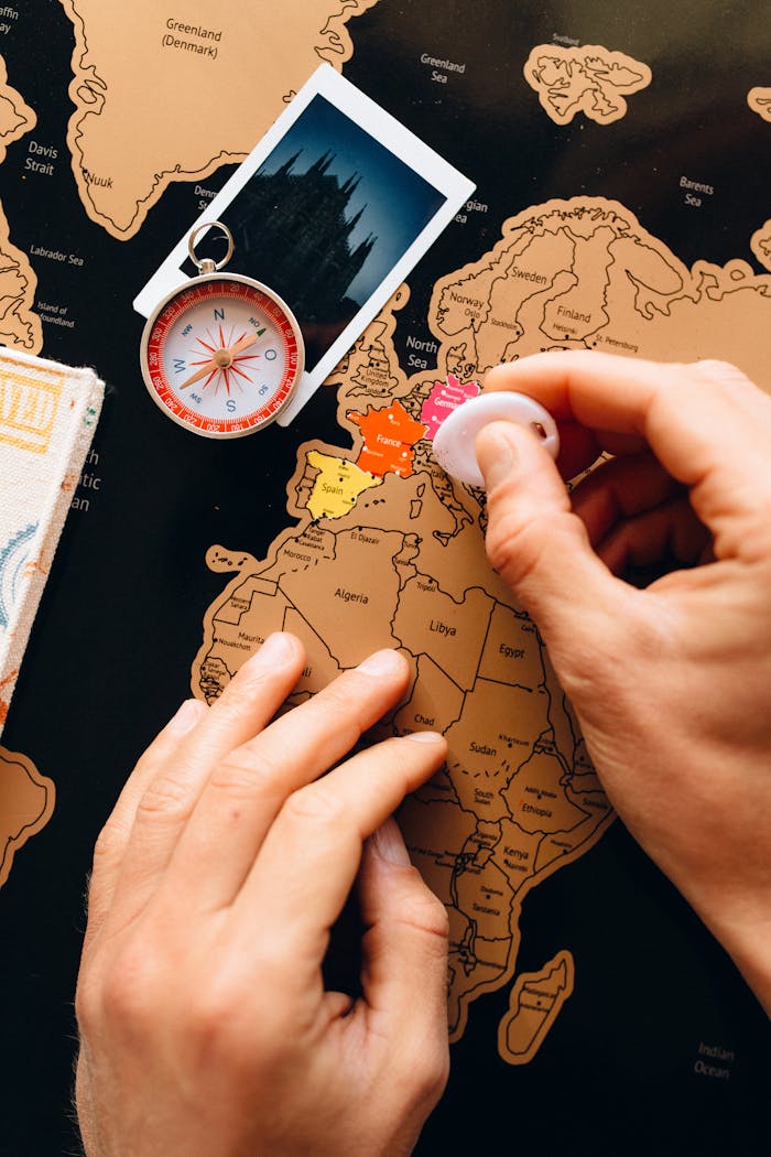 Close-up of hands scratching a travel map, featuring a compass and polaroid, symbolizing travel planning.