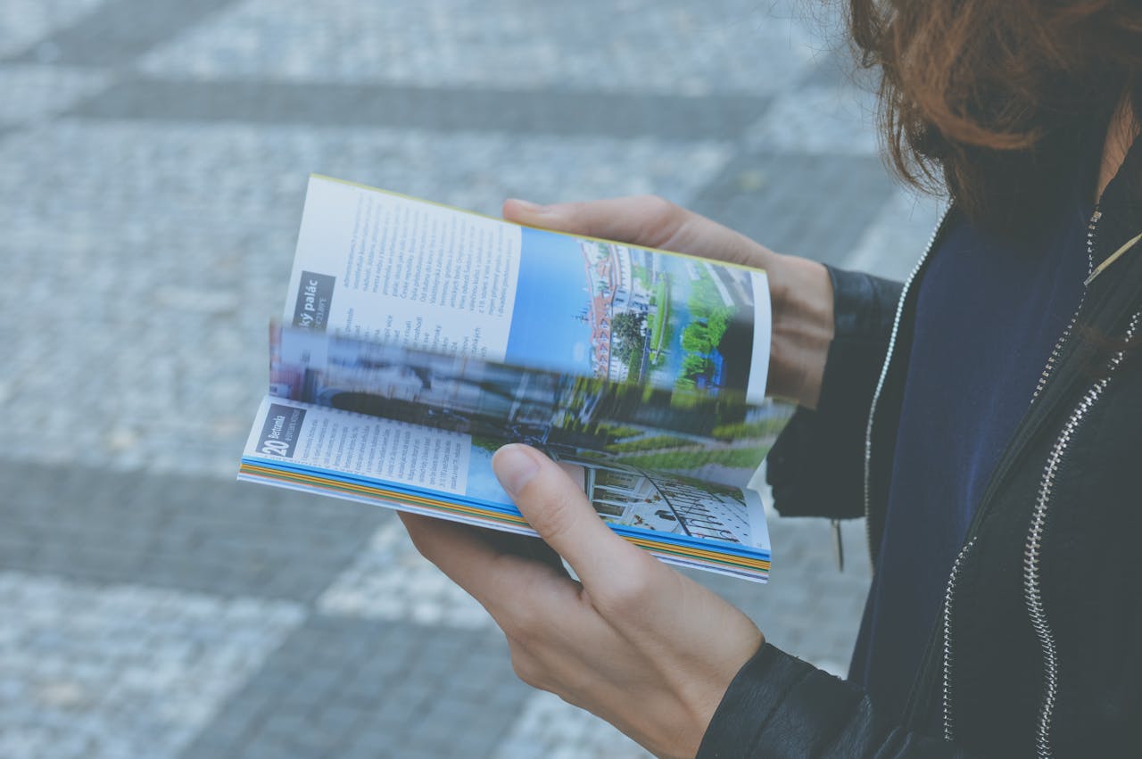 A person flipping through a travel book outdoors, showcasing a variety of vibrant pages.